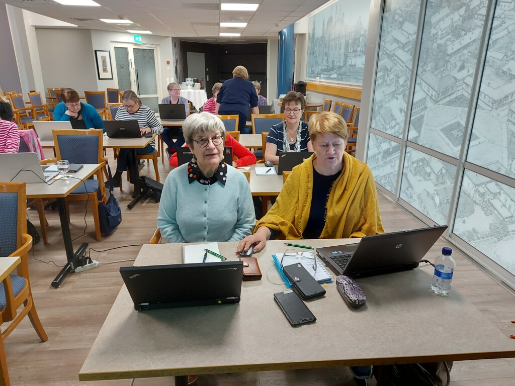 Osallistujia Eläkeliiton digikoulutuksessa Raahessa, etualalla kaksi naista läppäreiden kanssa.