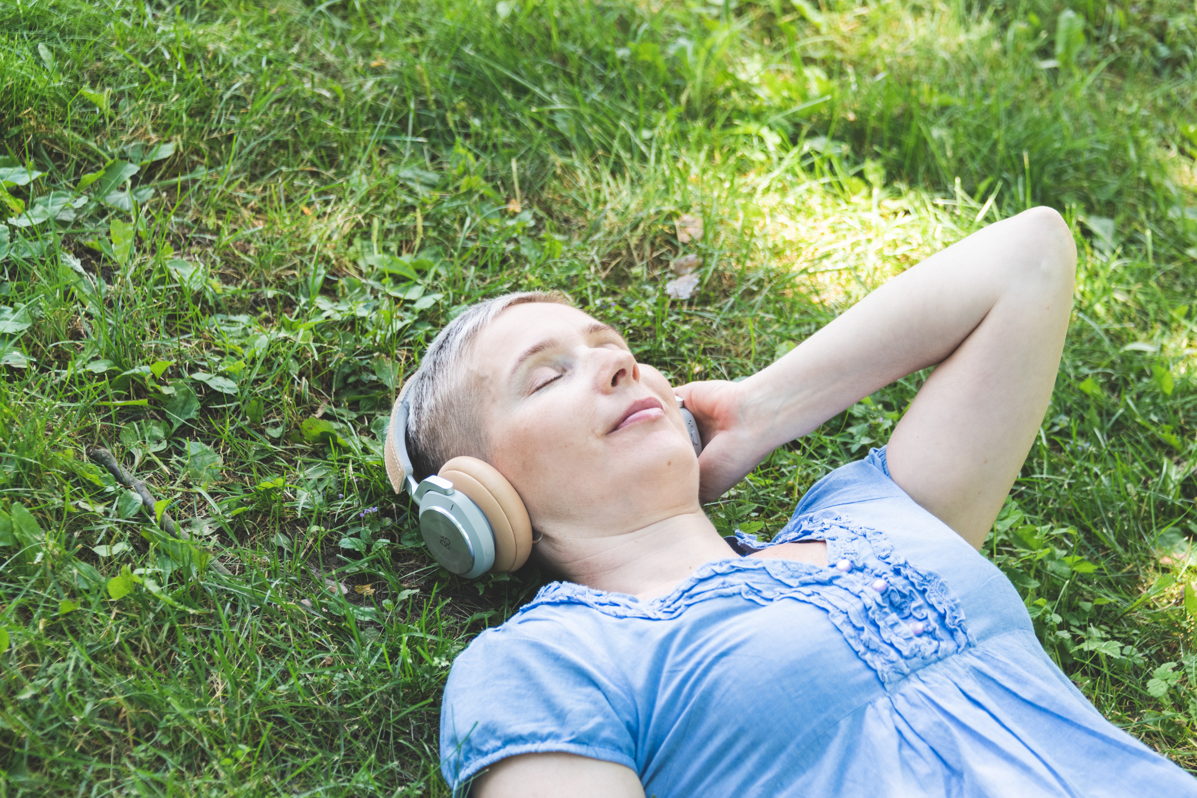 nainen löhöilee ruohikolla kuulokkeet korvillaan